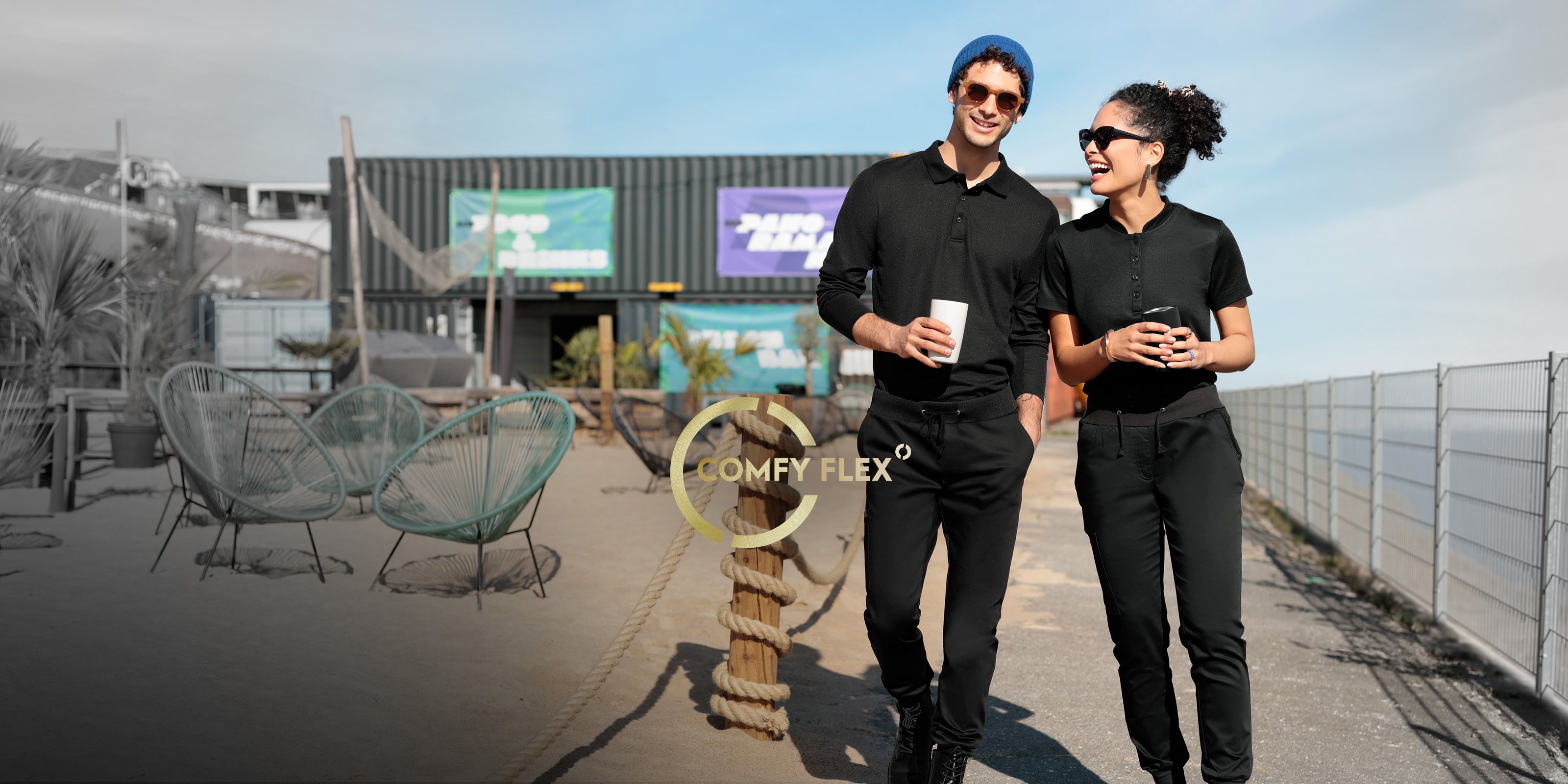 Deux personnes portant des tenues professionnelles COMFY FLEX noires, avec des boissons lors d’une pause en plein air.