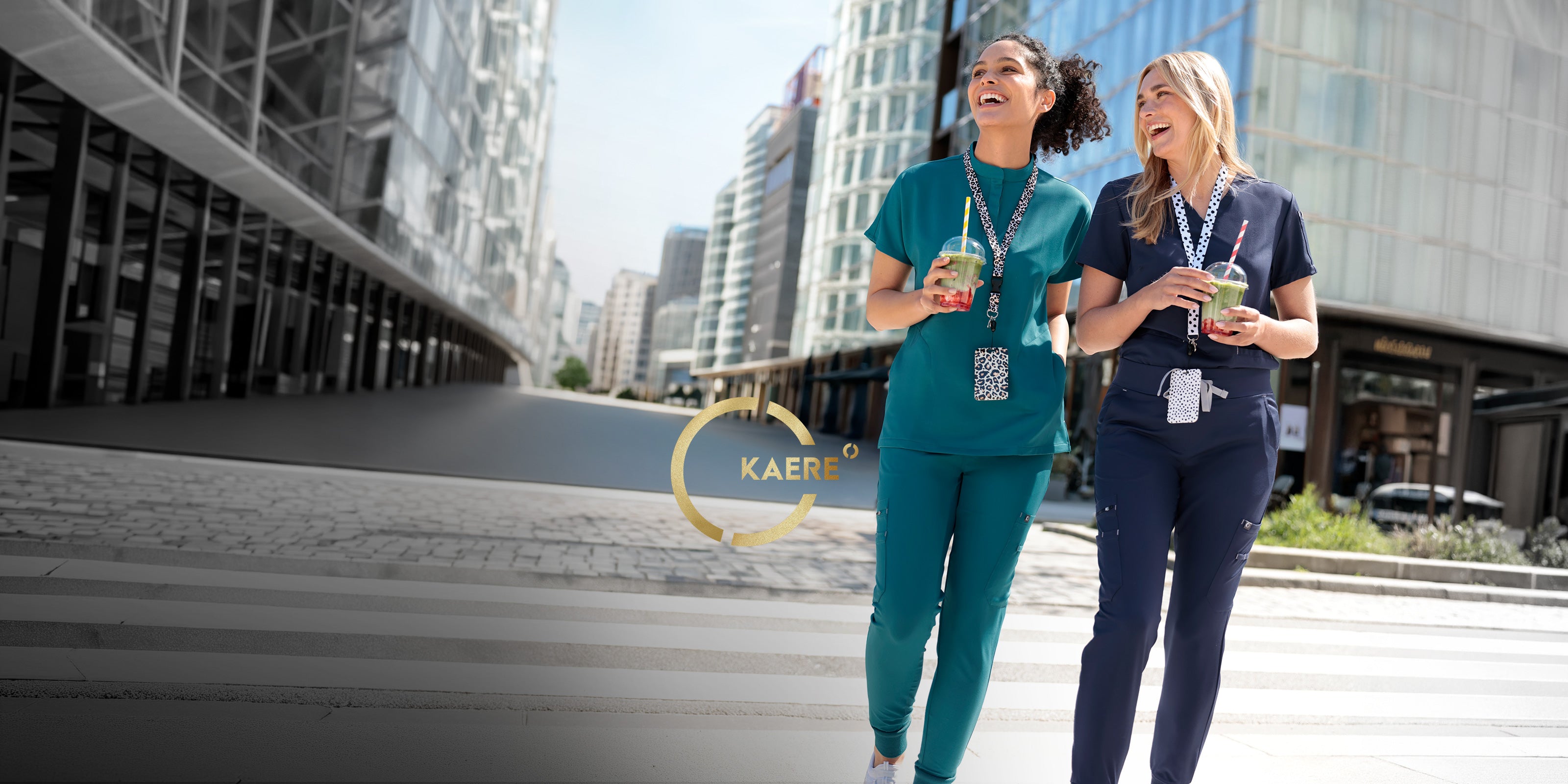 Deux femmes portant des tenues professionnelles KAERE turquoise et bleu marine, avec des boissons dans un décor urbain moderne.